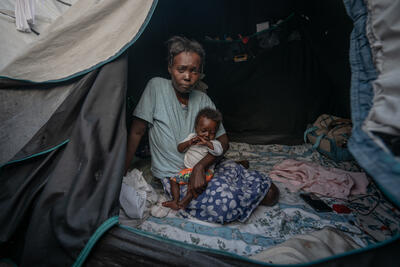 A woman sits inside an informal tent holding a baby in her arms.